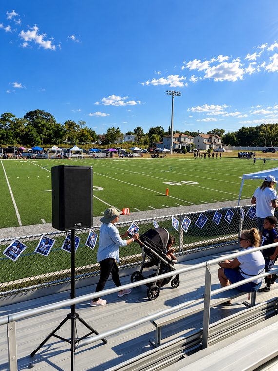 A tripod-mounted speaker providing coverage across stadium seating and an outdoor sports field.