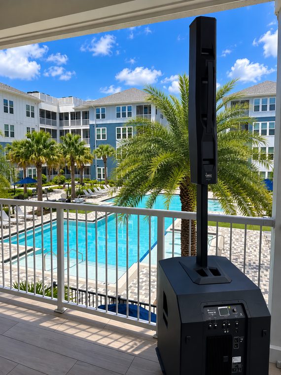 A column-array sound system and subwoofer positioned on a balcony above a pool courtyard.